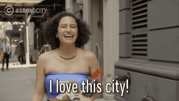 Woman in strapless top walks on street, laughing, with caption &quot;I love this city!&quot;