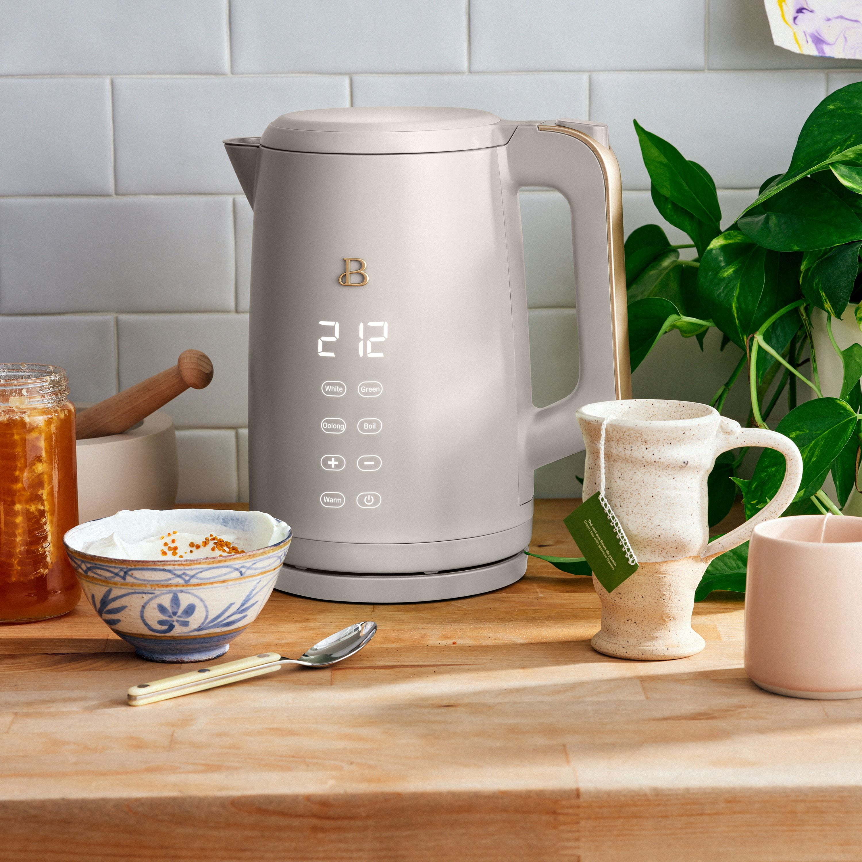Electric kettle on kitchen counter with digital display, alongside a bowl, mug, and spoon