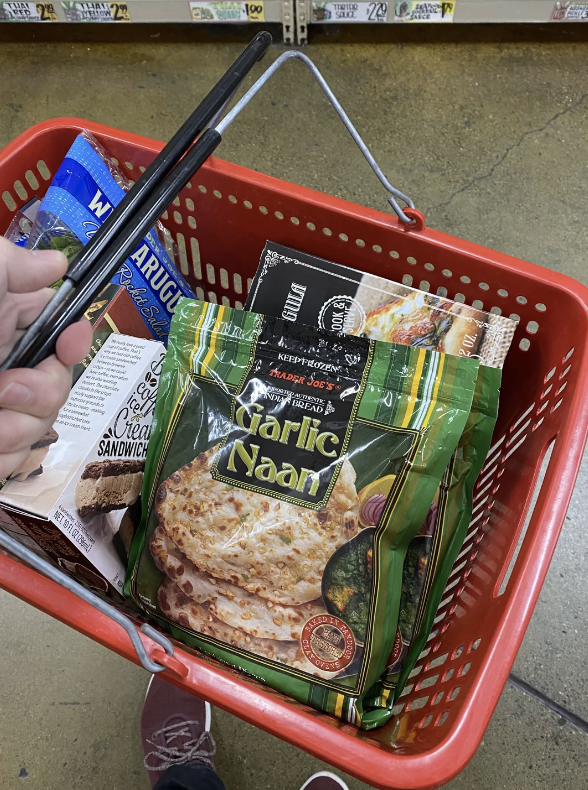 Person holding a red shopping basket filled with various grocery items, including garlic naan