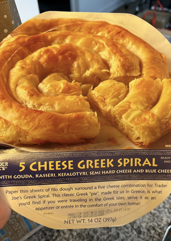 Hand holding a package of Trader Joe&#x27;s Spiral Cheese Pie with baking instructions visible