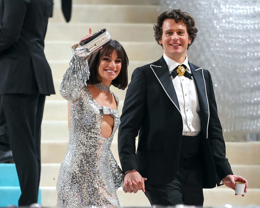 Lea in a sequined gown with cutouts and Jonathan in a black suit with a bow tie, holding hands at an event