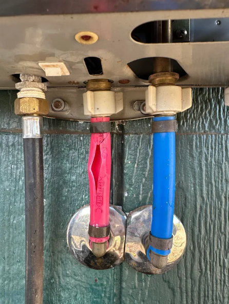 Burst pipes with red and blue handles for hot and cold water access, installed on a green wall