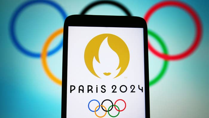 Logo of Paris 2024 Olympics displayed on a phone screen with Olympic rings in the background