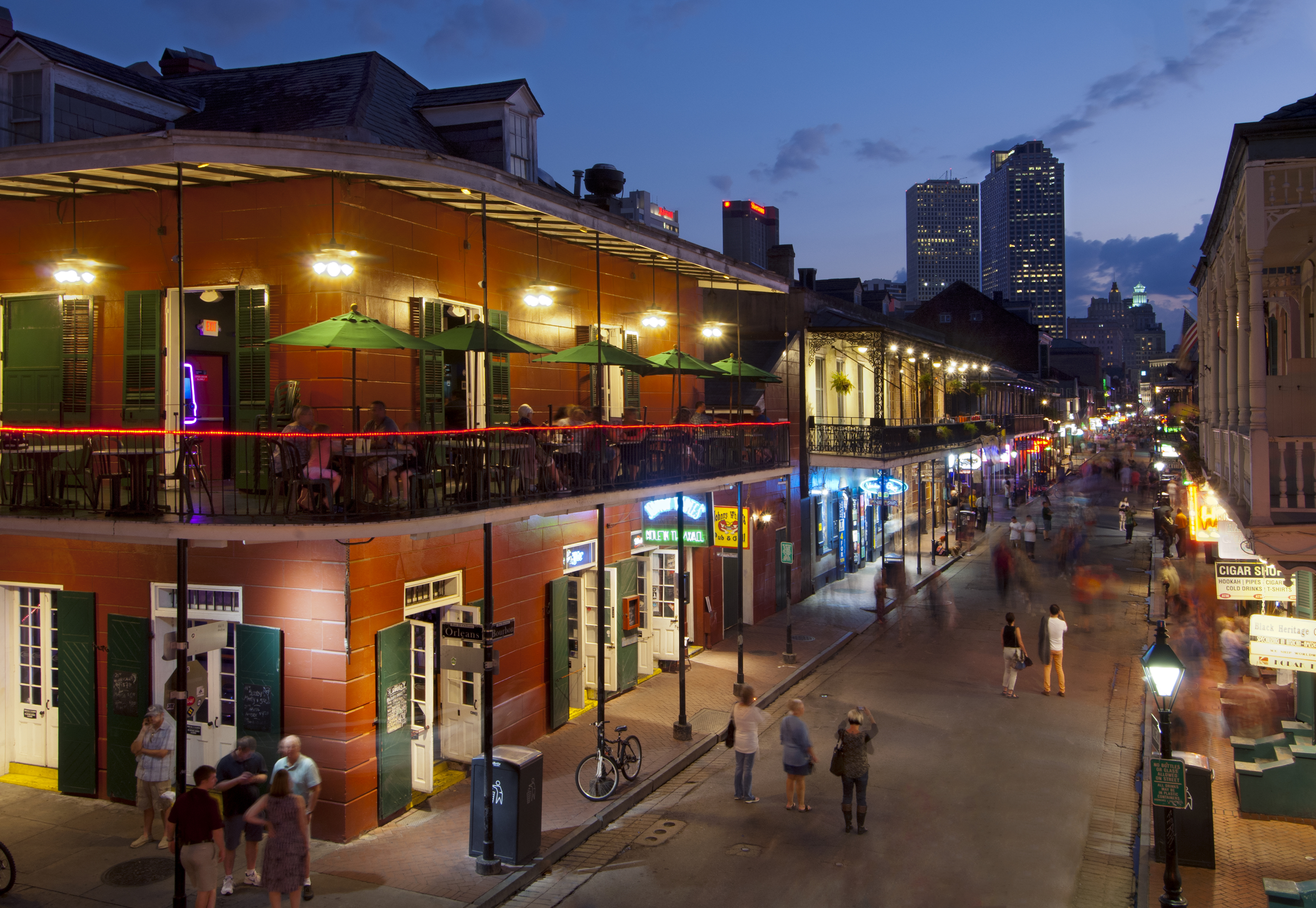 Bourbon Street in New Orleans at dusk, busy with pedestrians and illuminated buildings