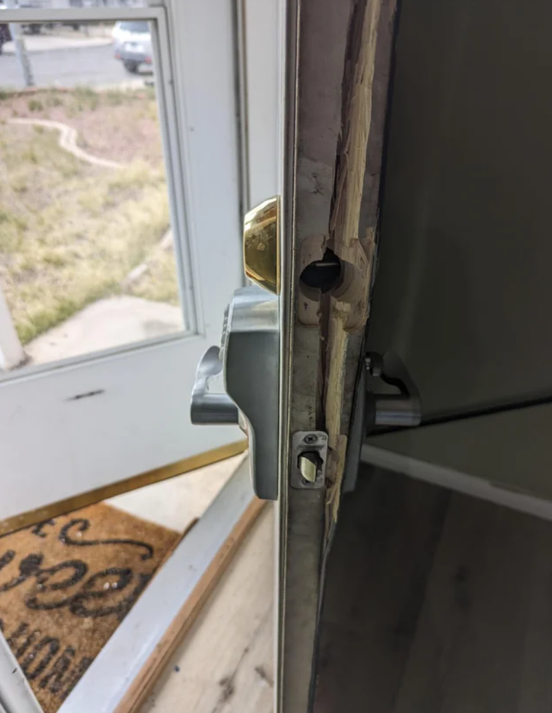 A close-up of a door latch mechanism, slightly open, with a view of the outdoors through the gap