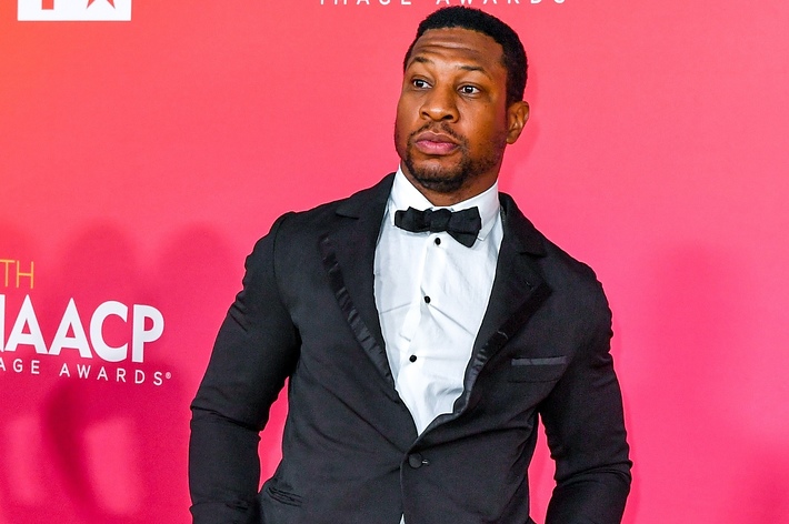 Man in a tuxedo with bowtie standing before a backdrop with text '54th NAACP Image Awards'