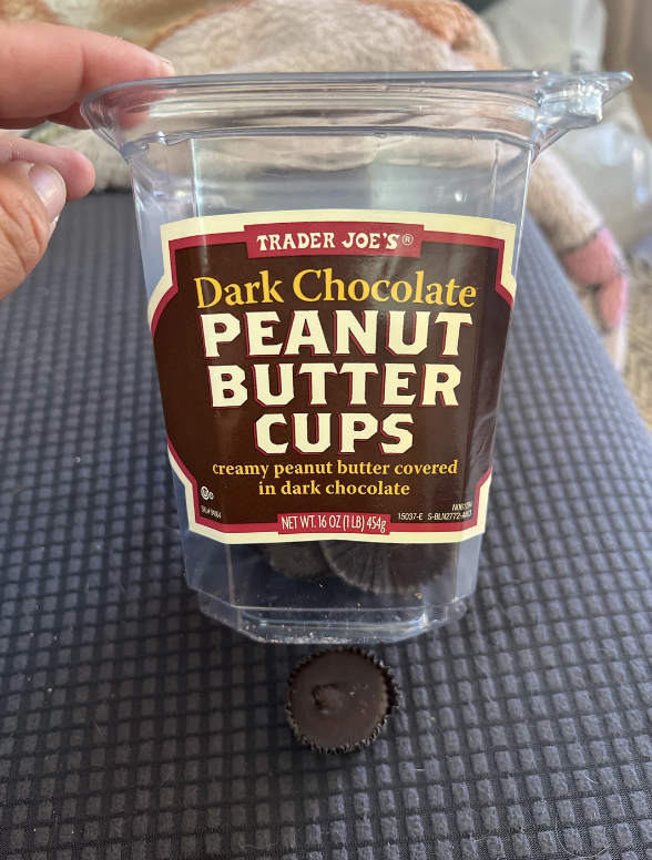 Hand holding a container of Trader Joe&#x27;s Dark Chocolate Peanut Butter Cups with one piece visible