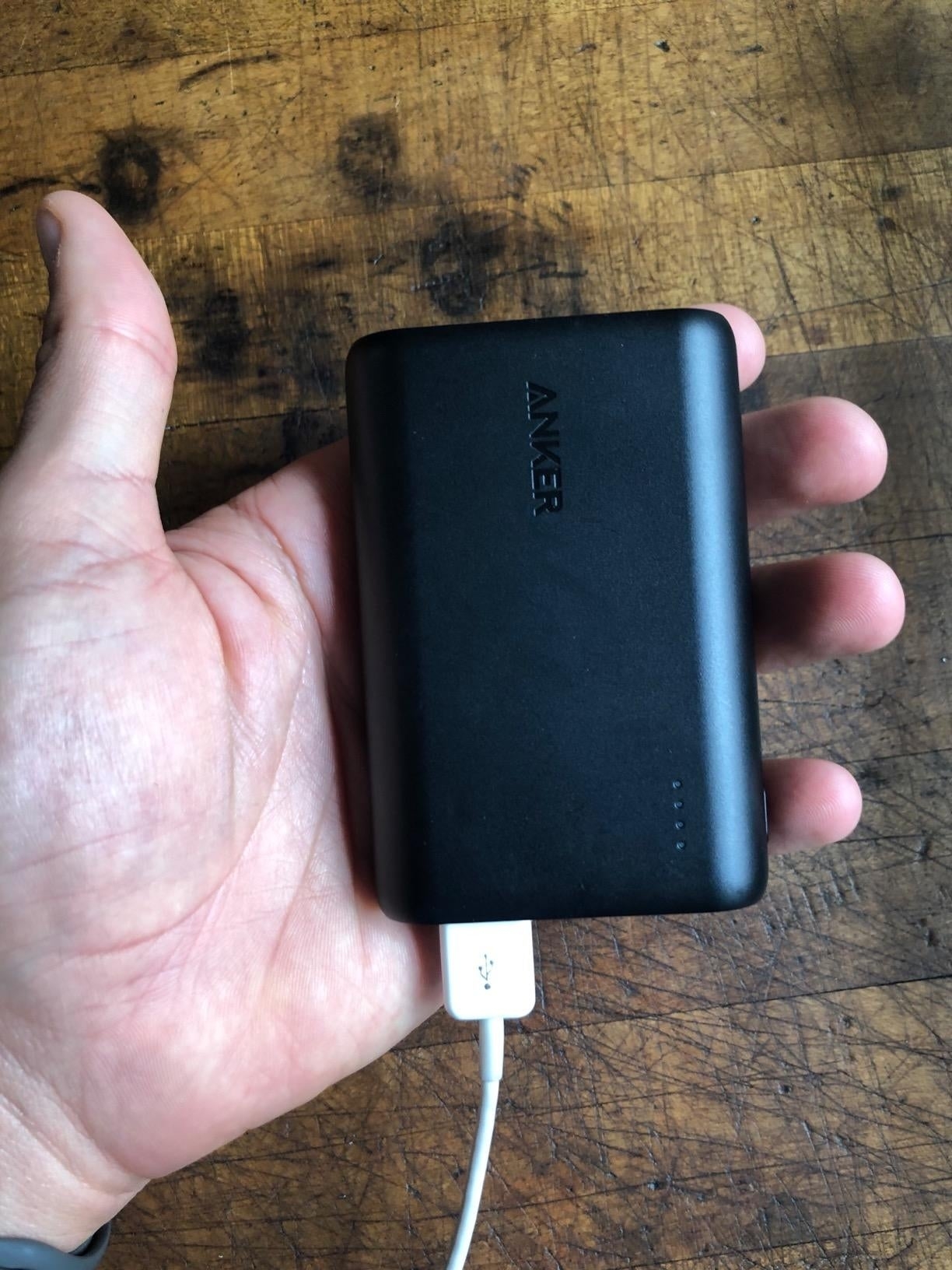 Hand holding a portable Anker power bank with a charging cable attached