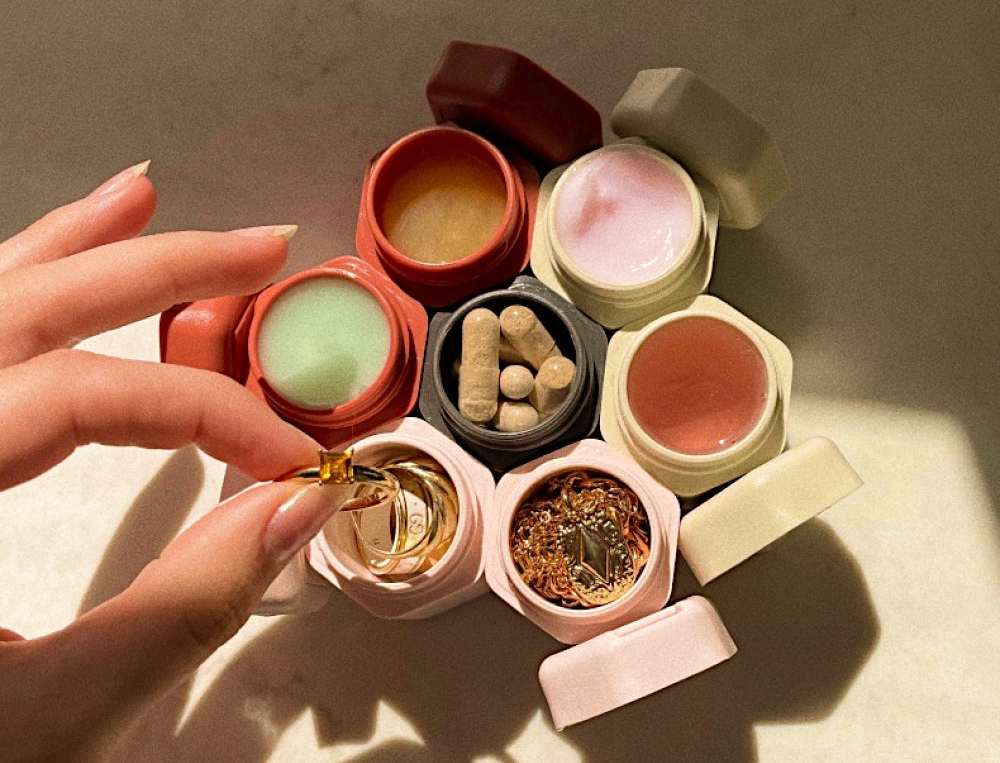 Person&#x27;s hand holding a ring beside open jars of various cosmetic products