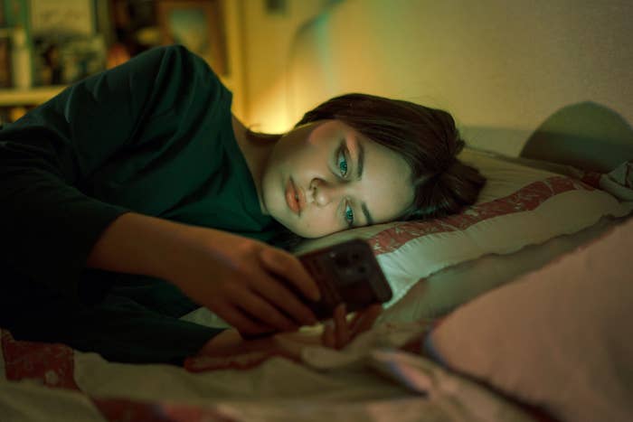 Person lying on bed looking at smartphone screen in dimly lit room