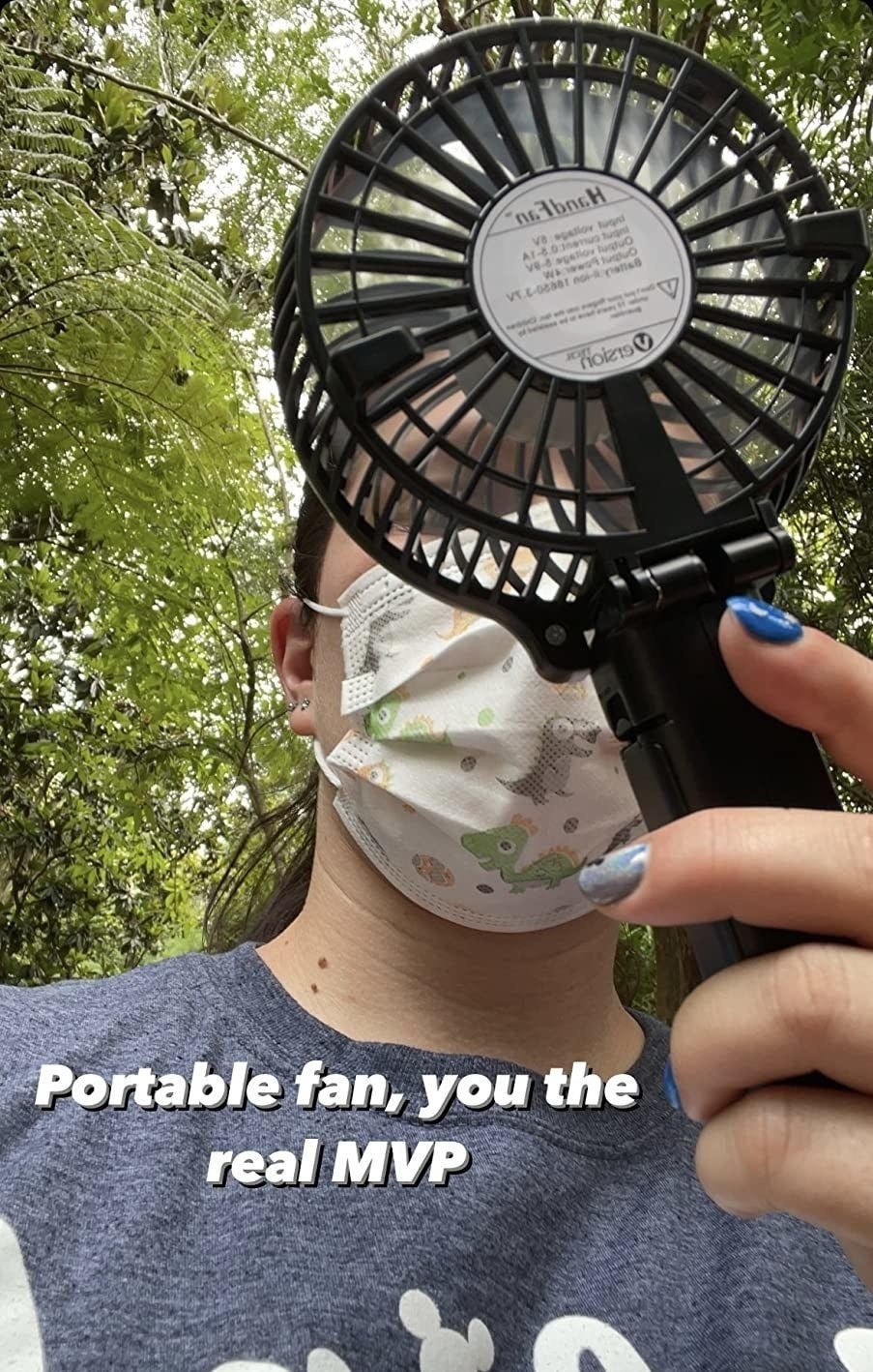 Person holding a portable fan near their face, wearing a mask and t-shirt, with trees in the background. Text on image: &quot;Portable fan, you the real MVP.&quot;