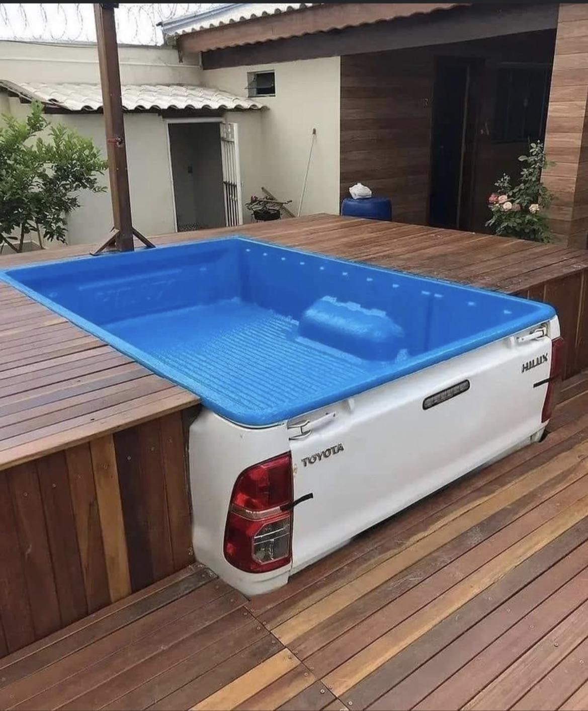A Toyota Hilux truck bed converted into an above-ground pool with wooden decking around it