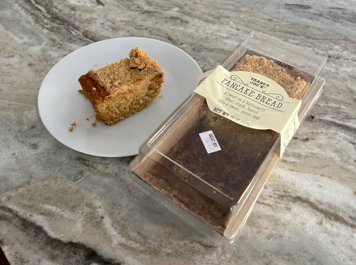 A slice of cake on a plate beside its packaging labeled &quot;Vintage Bread Pineapple Bread&quot; on a marble surface