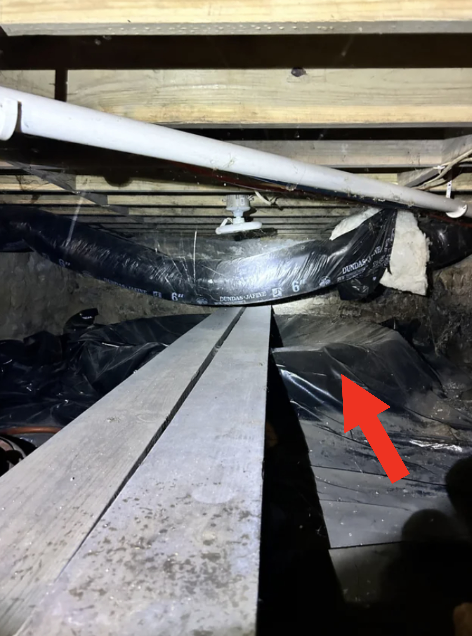 Crawl space under a house with wooden planks, pipes, and covered soil