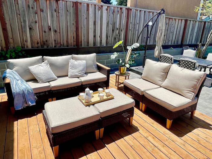Outdoor seating area with a sofa, chairs, and a table under sunlight, with a potted plant and cushions on the furniture