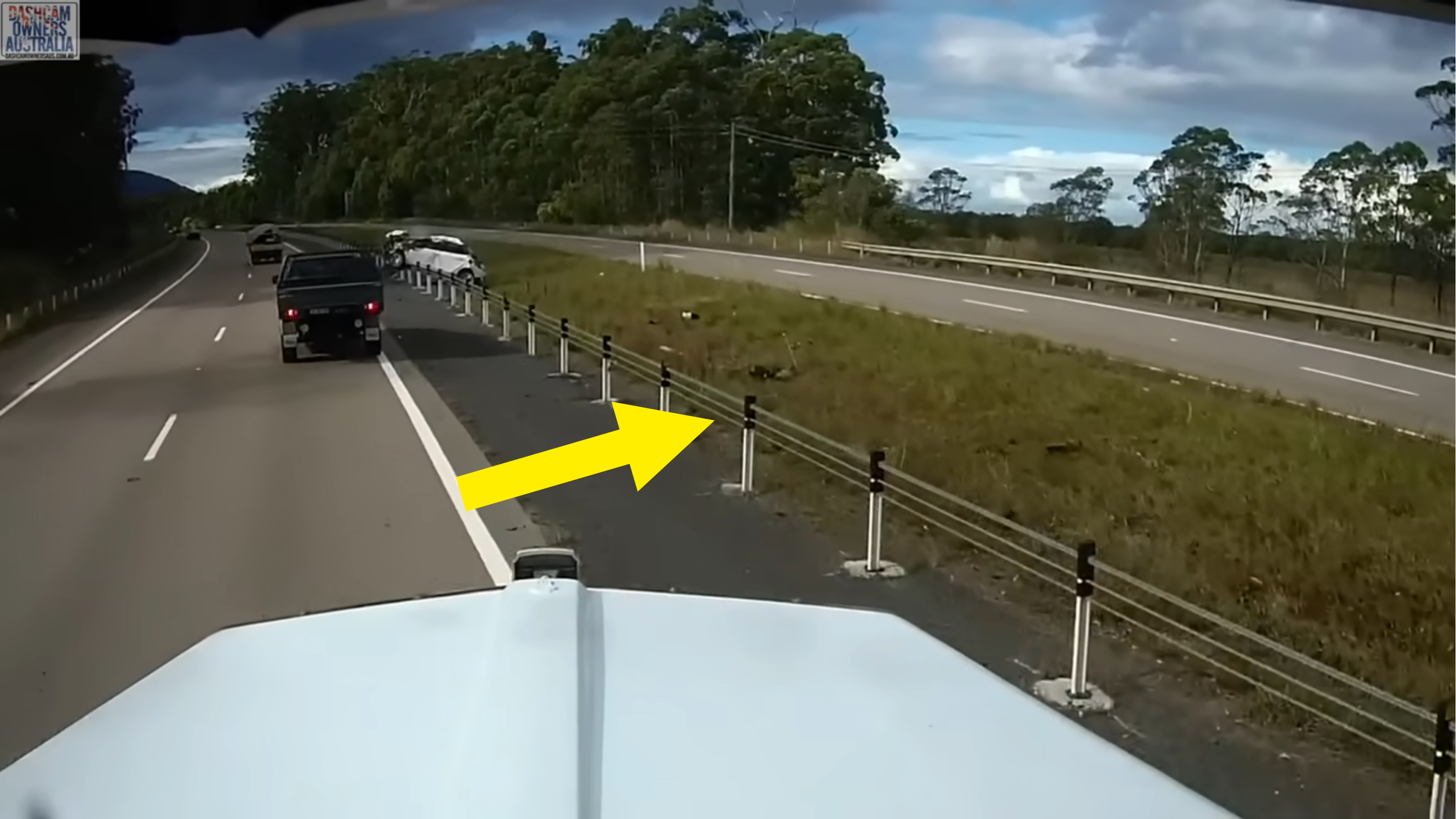 Dashcam view from vehicle showing another car passing by on a highway with guardrails and grassy verge