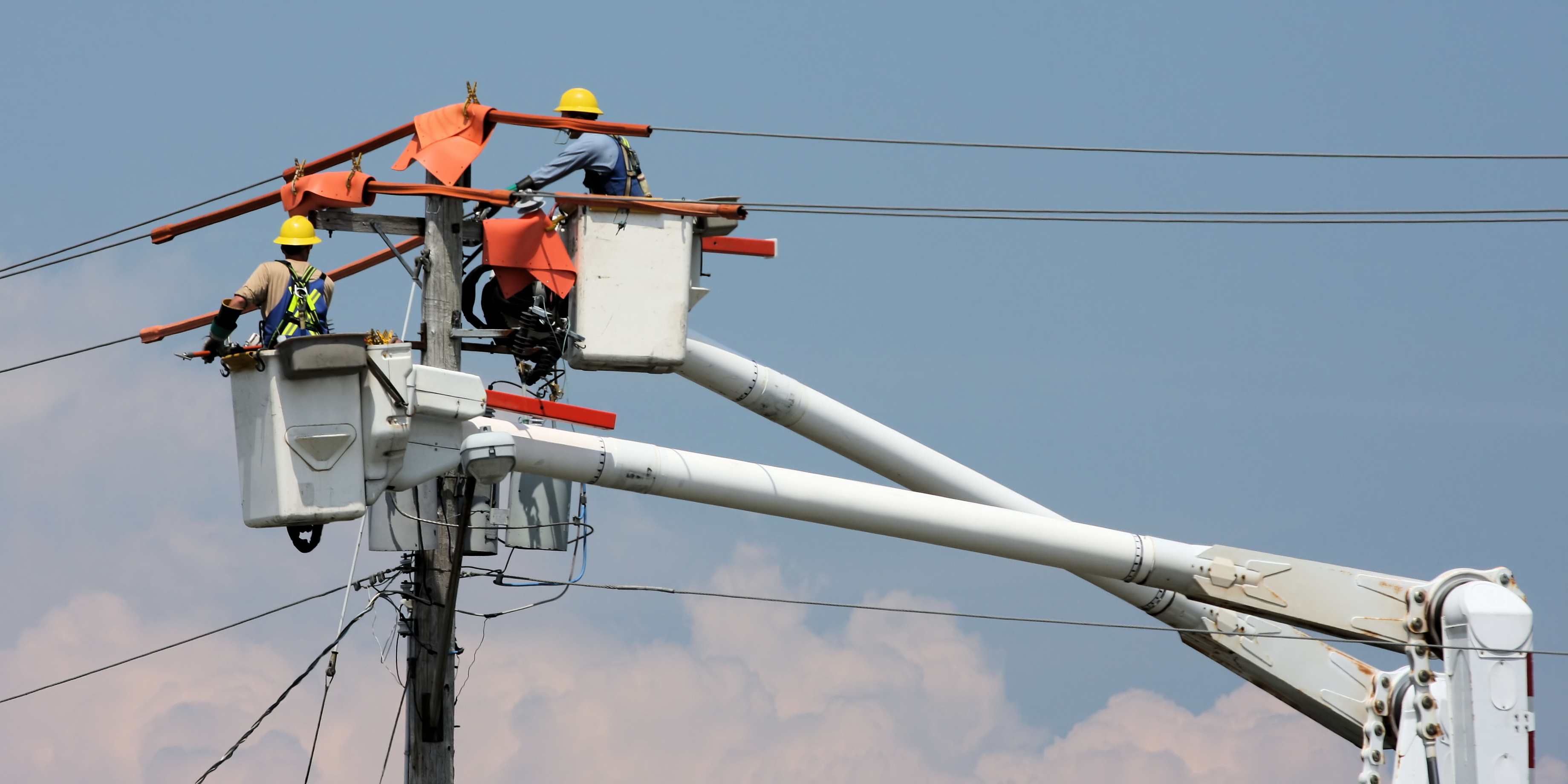 Two utility workers repairing lines from elevated bucket trucks