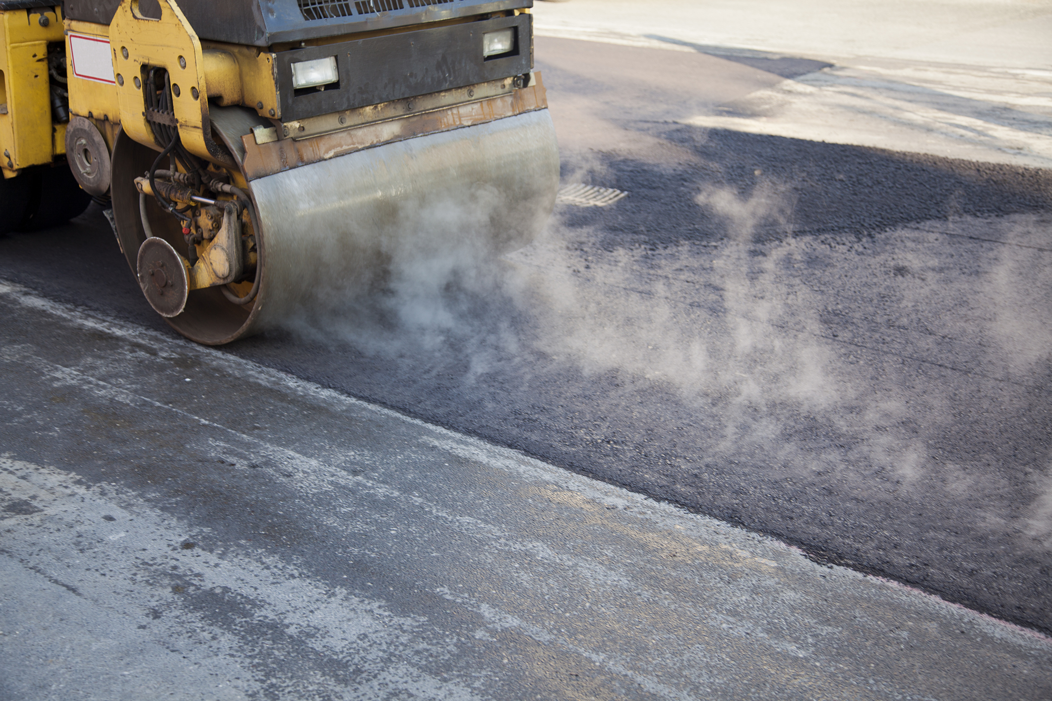 Road roller smoothing asphalt with steam rising during road construction. No people visible