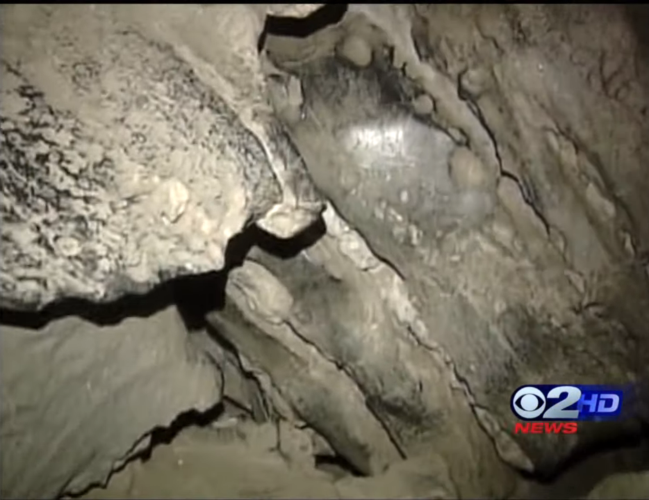 Camera footage of a rocky underground cave structure with visible formations, from a 02 HD News segment