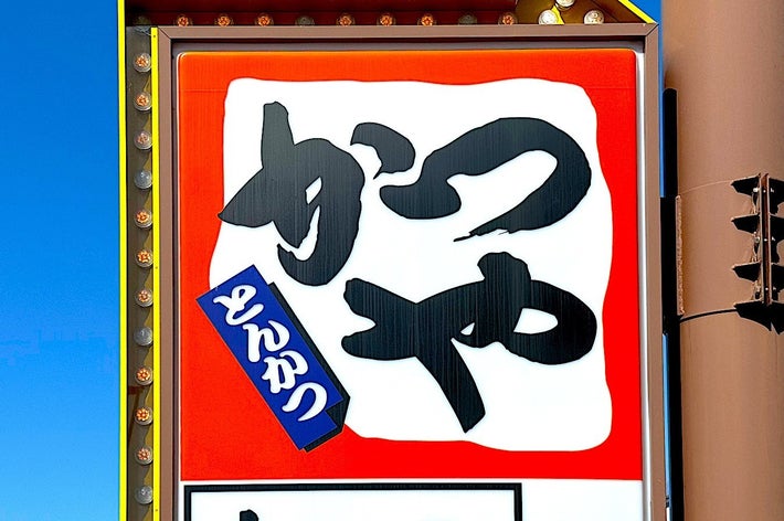 Signboard with large Japanese characters, smaller text beneath, against a sky backdrop