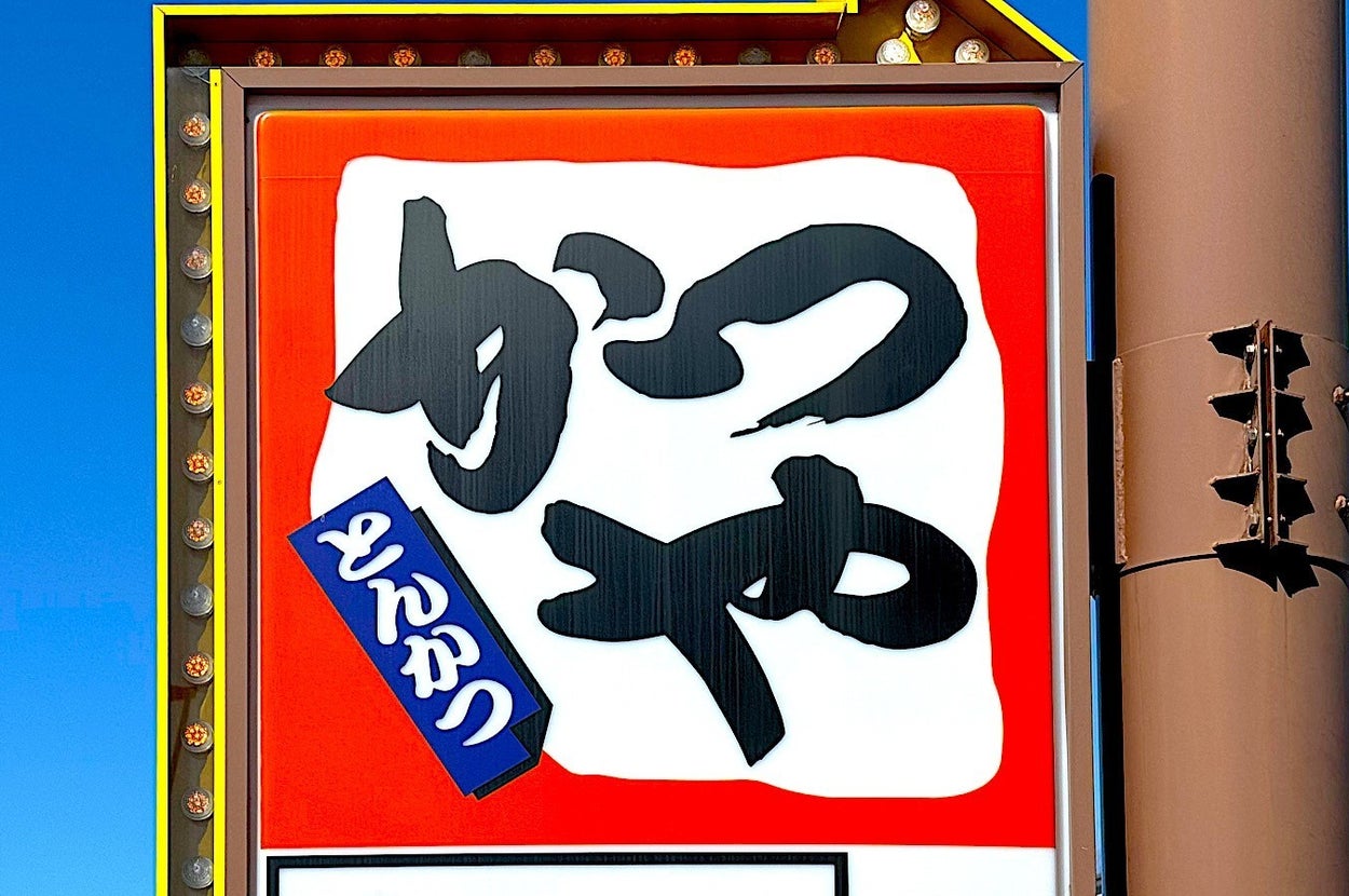 Signboard with large Japanese characters, smaller text beneath, against a sky backdrop