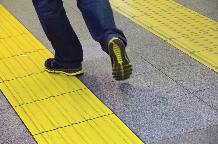 人が黄色い点字ブロックを歩いている。