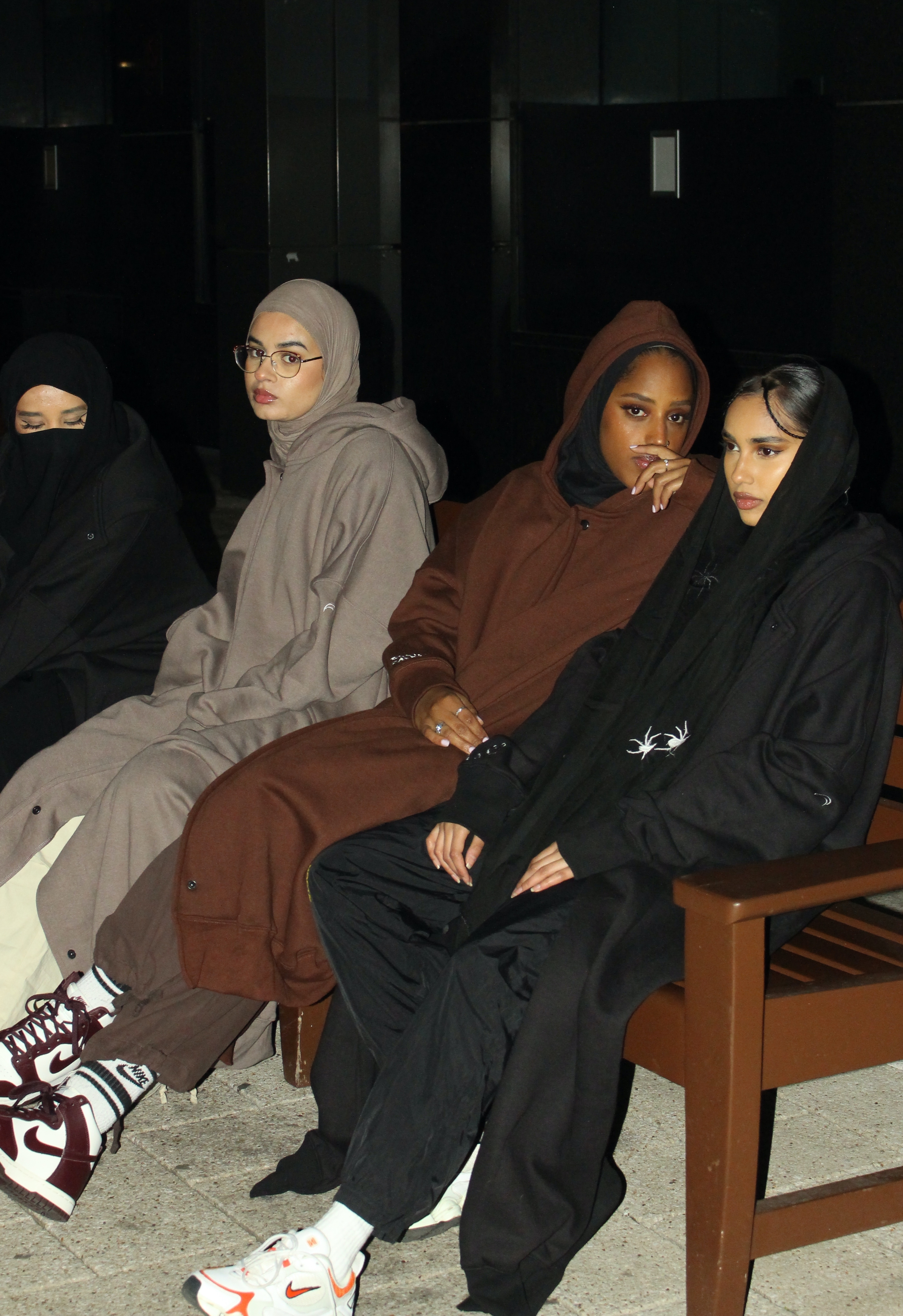 Four women wearing hijabs and hoodie abayas seated together on a bench