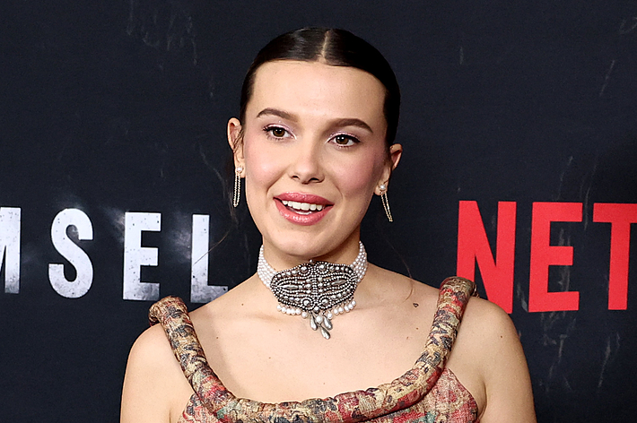 Celebrity in a patterned tank top and jeans with a statement necklace, posing at a Netflix event