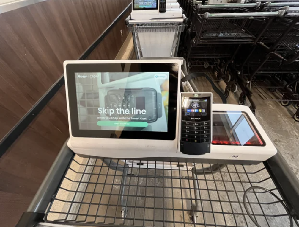 Self-checkout kiosk screen reads &quot;Skip the line&quot; with a barcode scanner and payment terminal adjacent