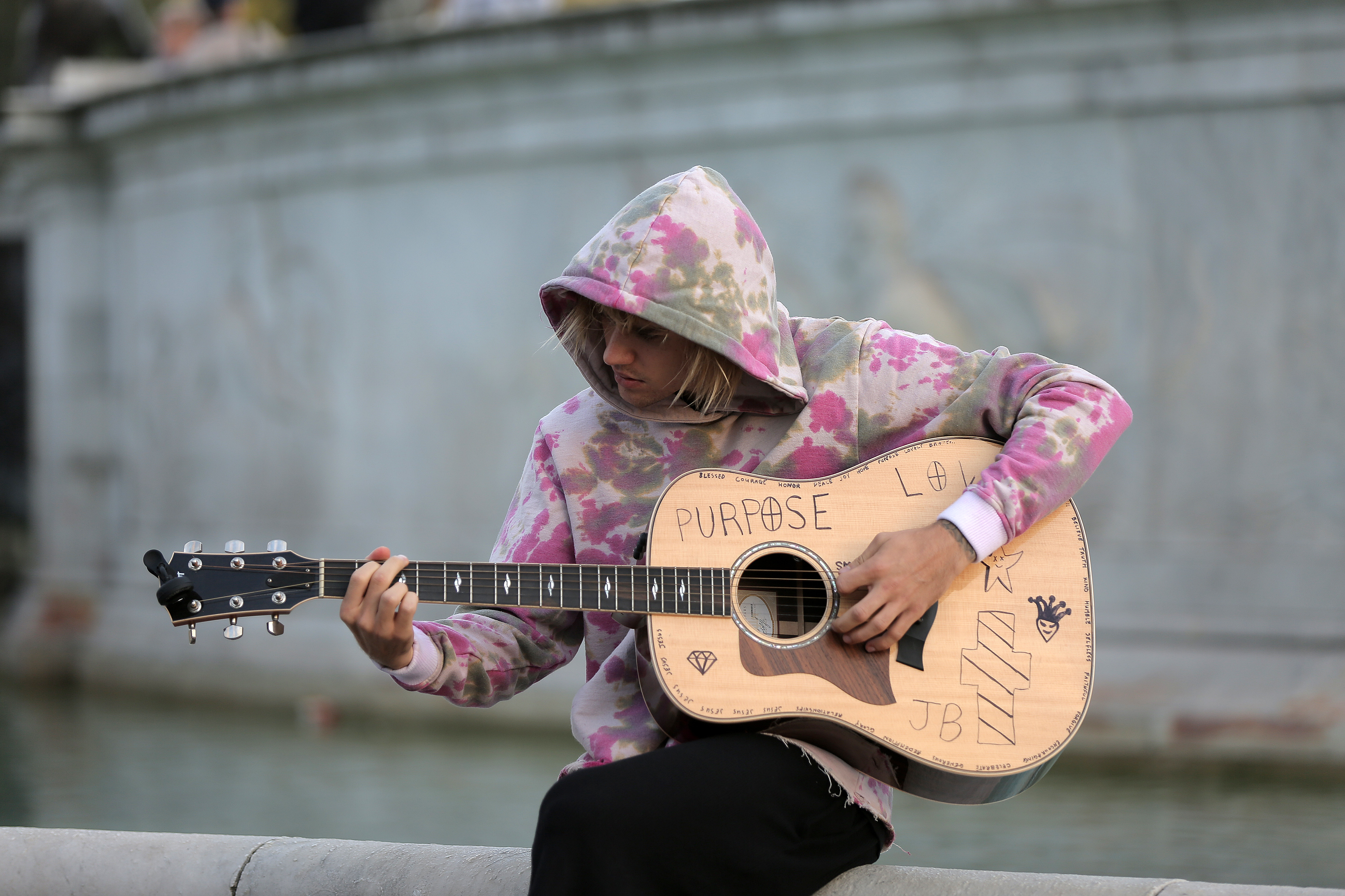 justin in a hoodie playing a guitar outside