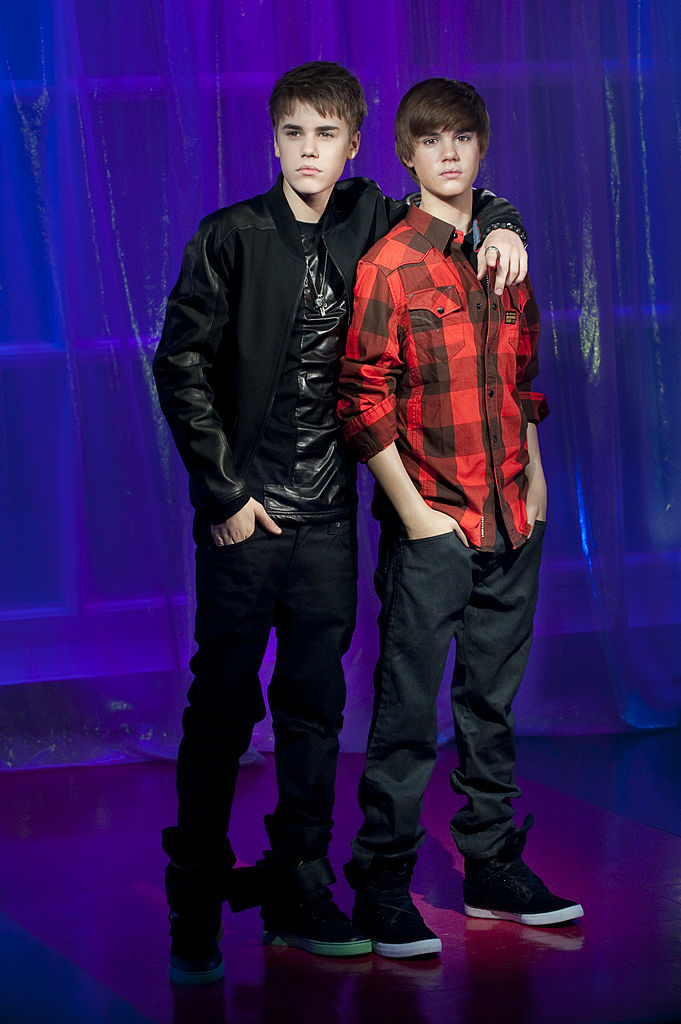 Justin Bieber posing with his arm around his wax figure, he’s young and his his hair swept to the side