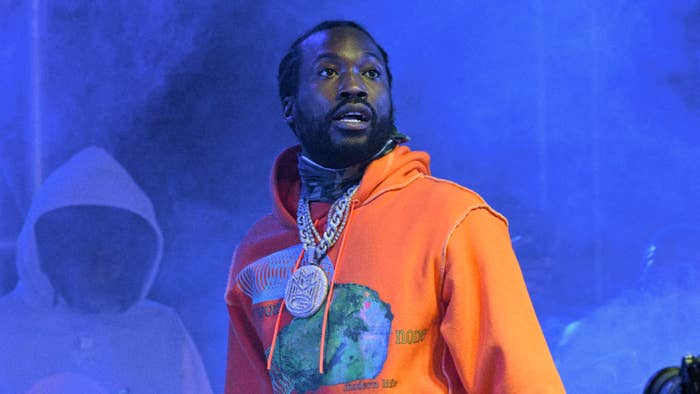 Meek Mill in orange hoodie and chain necklaces performing on stage