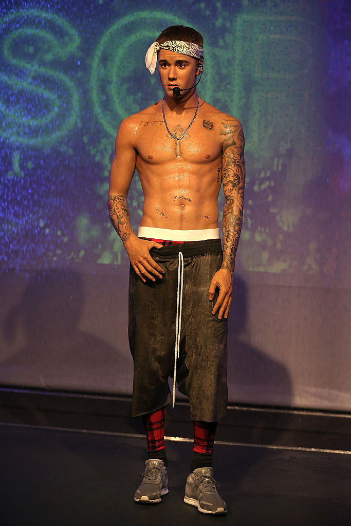 Shirtless wax figure with tattoos, headband, and baggy pants posing on a stage