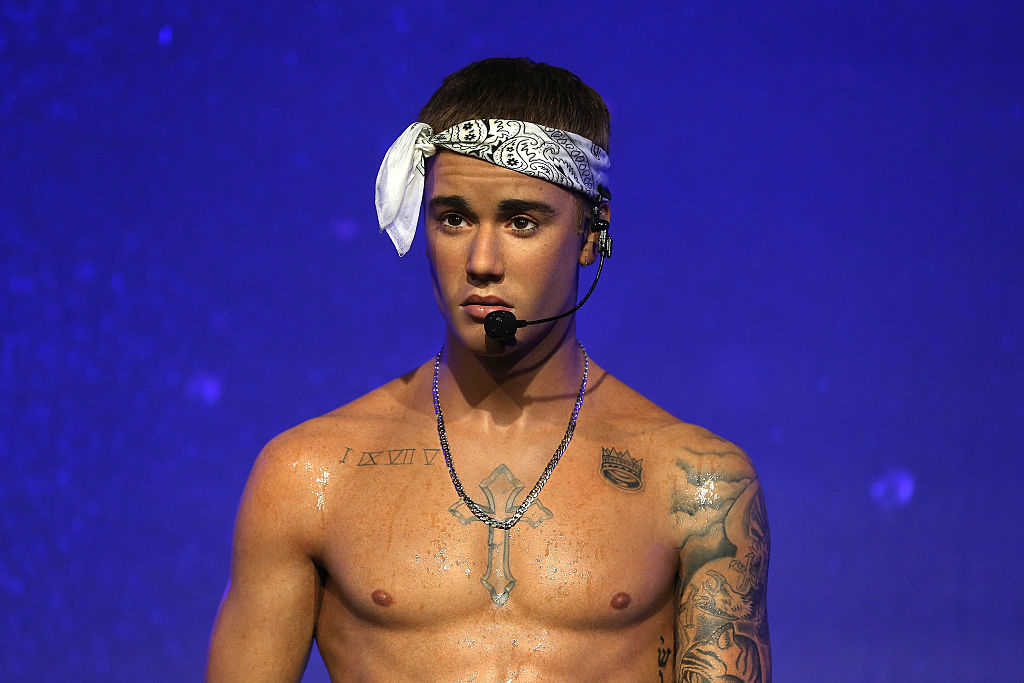Justin Bieber wearing a headband and a mic, shirtless, tattoos visible