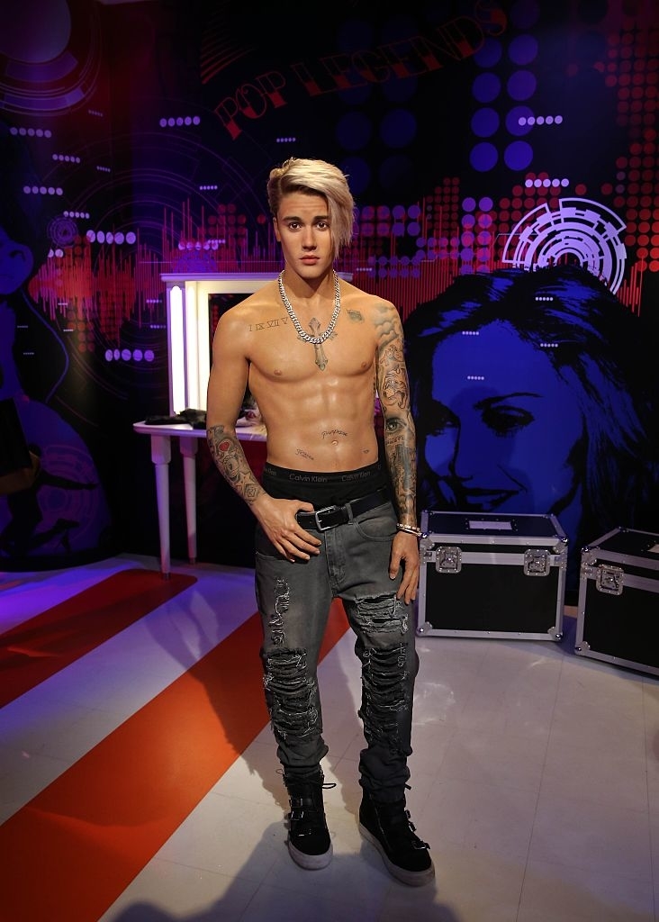 Wax figure of Justin Bieber standing shirtless with tattoos visible, wearing ripped jeans