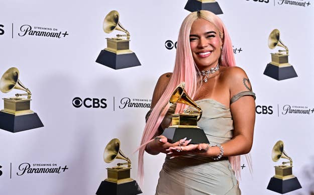 Karol G holding a Grammy Award, wearing an elegant strapless dress with a choker-style necklace