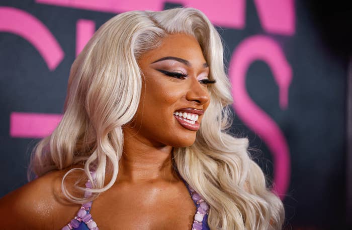 Megan Thee Stallion smiling at an event with a bejeweled pink top and blonde waves