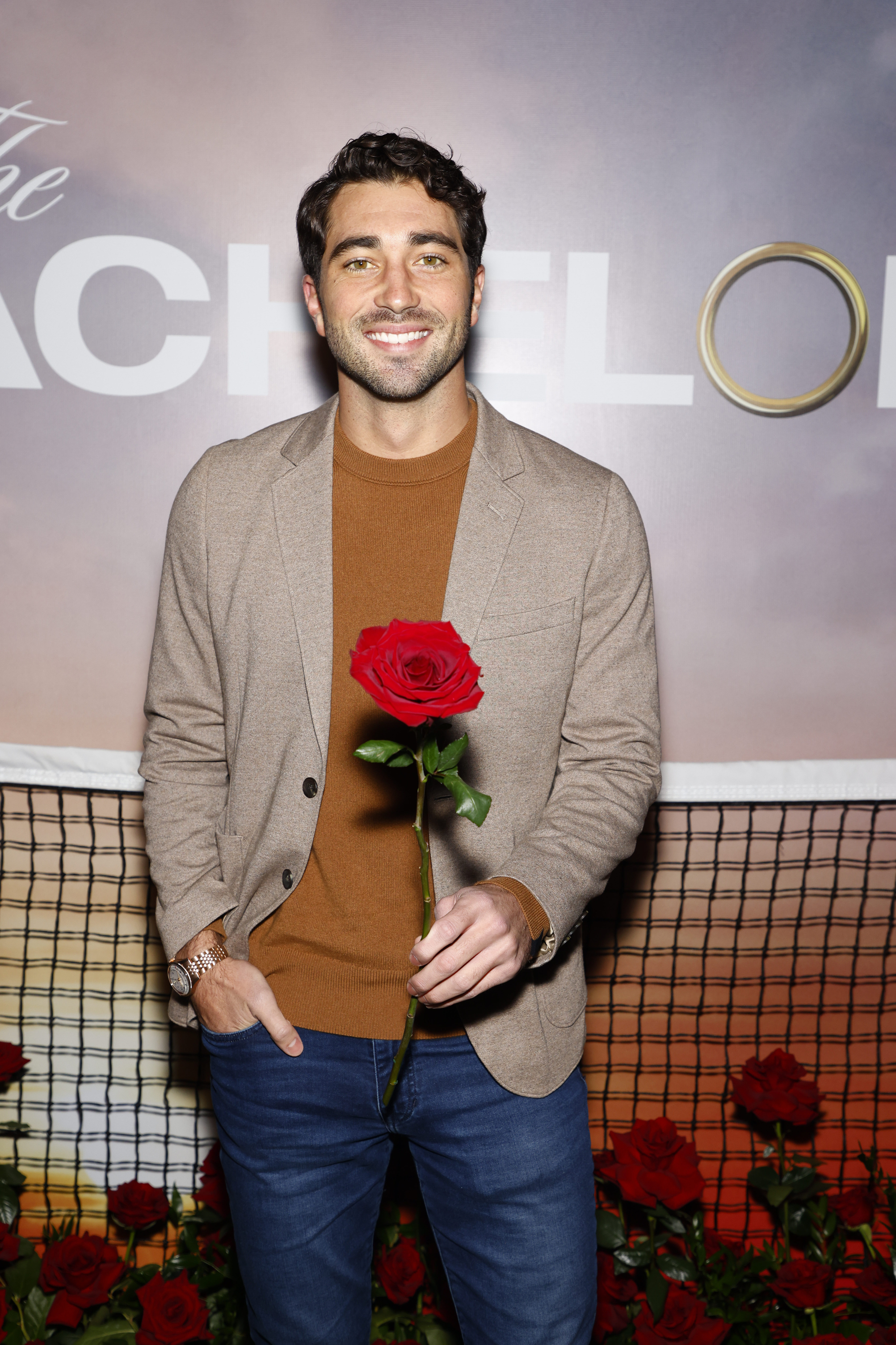 joey  in a blazer and sweater holding a rose