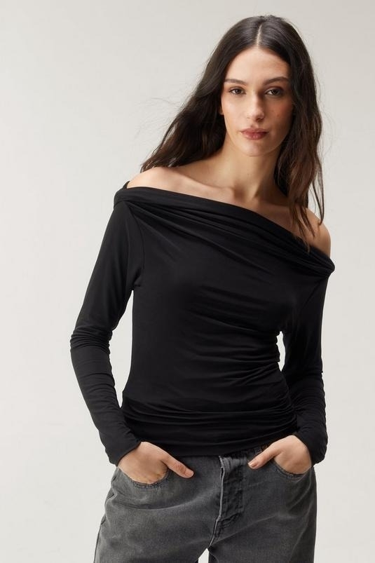 Woman in an off-the-shoulder black top and gray jeans posing with hands on hips