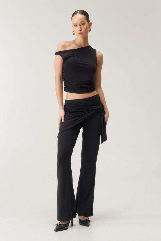 Model wearing an asymmetrical black top with matching pants, paired with heeled sandals