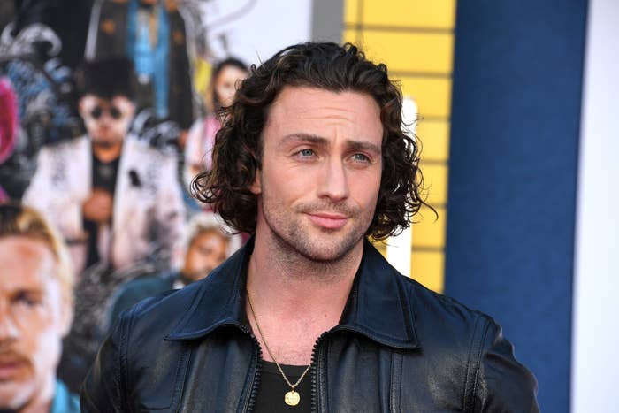 Man with curly hair in a leather jacket posing at an event