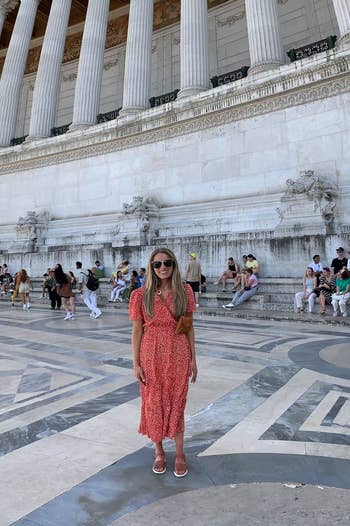 Woman in a patterned dress standing in front of a historical building with columns, tourists in the background
