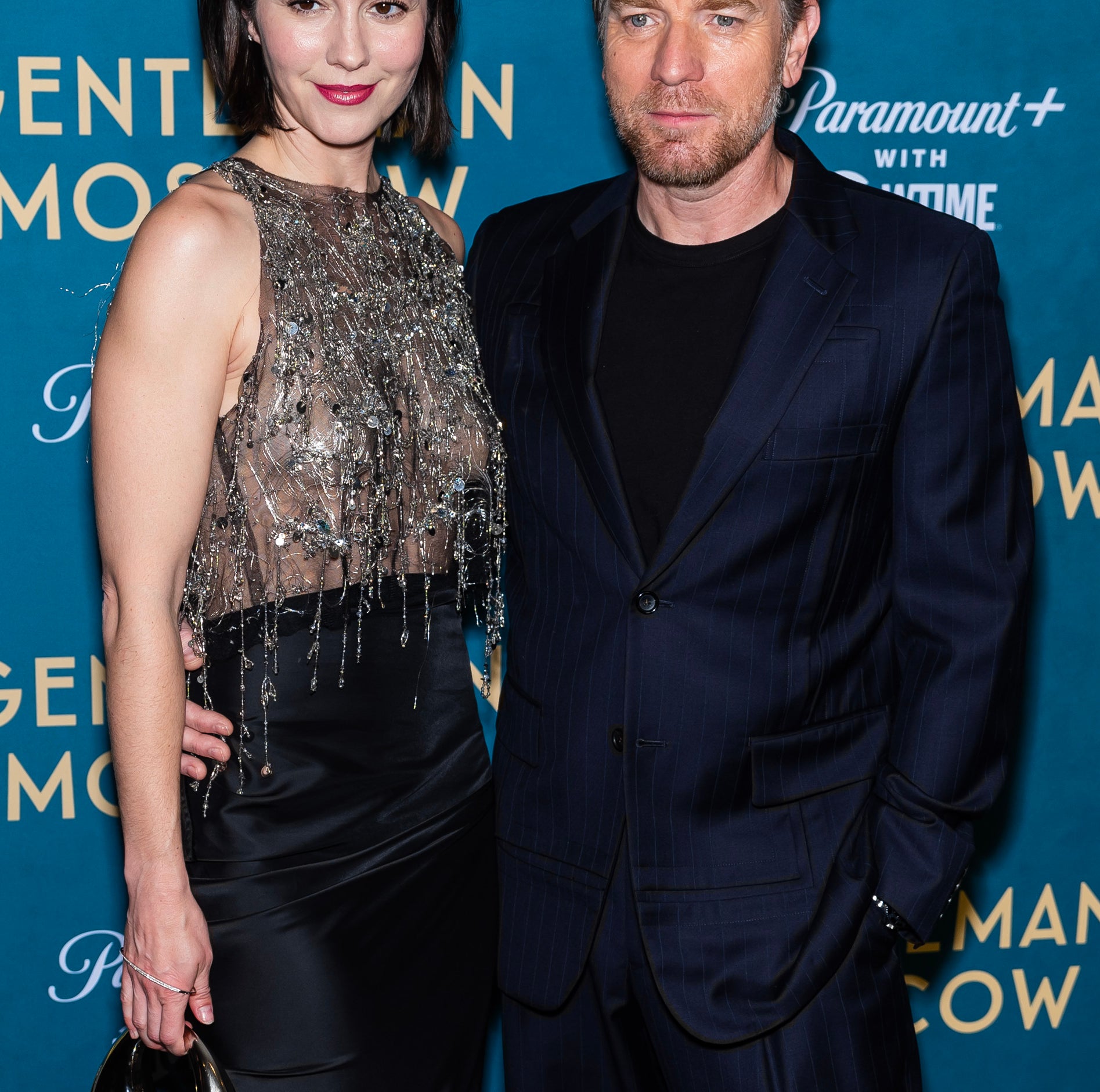 Ewan McGregor and Mary Elizabeth Winstead posing together at an event. She wears a beaded top and skirt; he sports a pinstripe suit