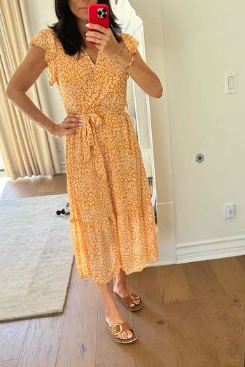 Person in a patterned wrap dress with tie waist and open-toed sandals, taking a mirror selfie