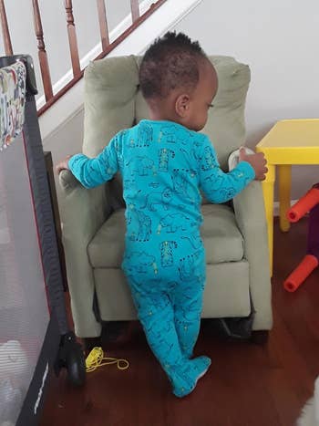 Toddler successful patterned pajamas lasting against a tiny armchair, facing away, successful a location setting