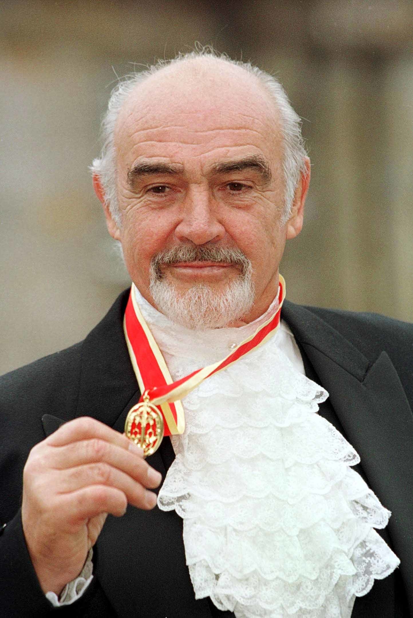 Man with a medal, wearing a suit and frilled cravat, smiling at the camera