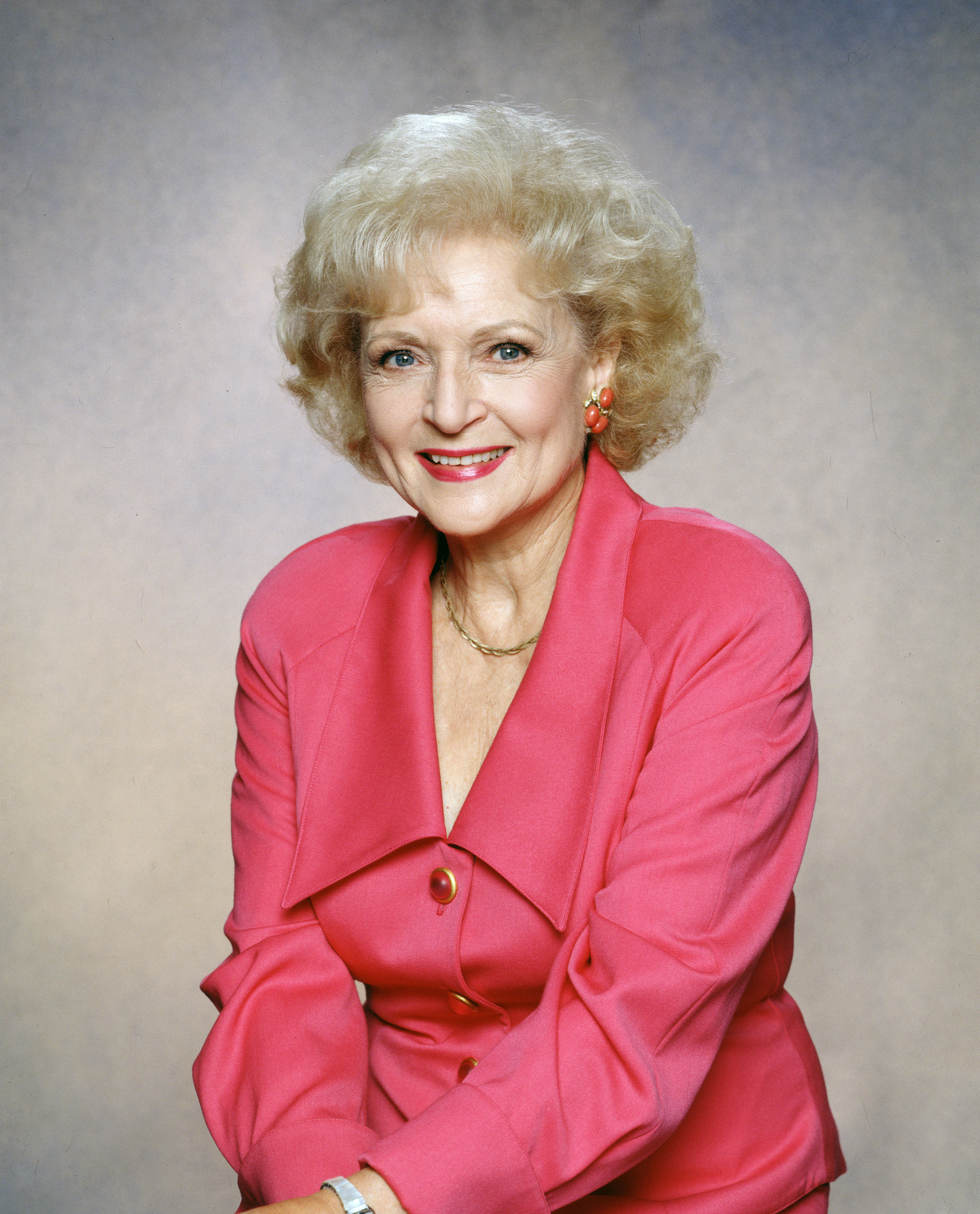 Betty White poses smiling in a buttoned pink blazer with lapels and matching earrings