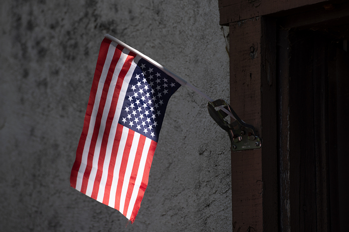 An American flag hangs from a metallic bracket on a textured wall
