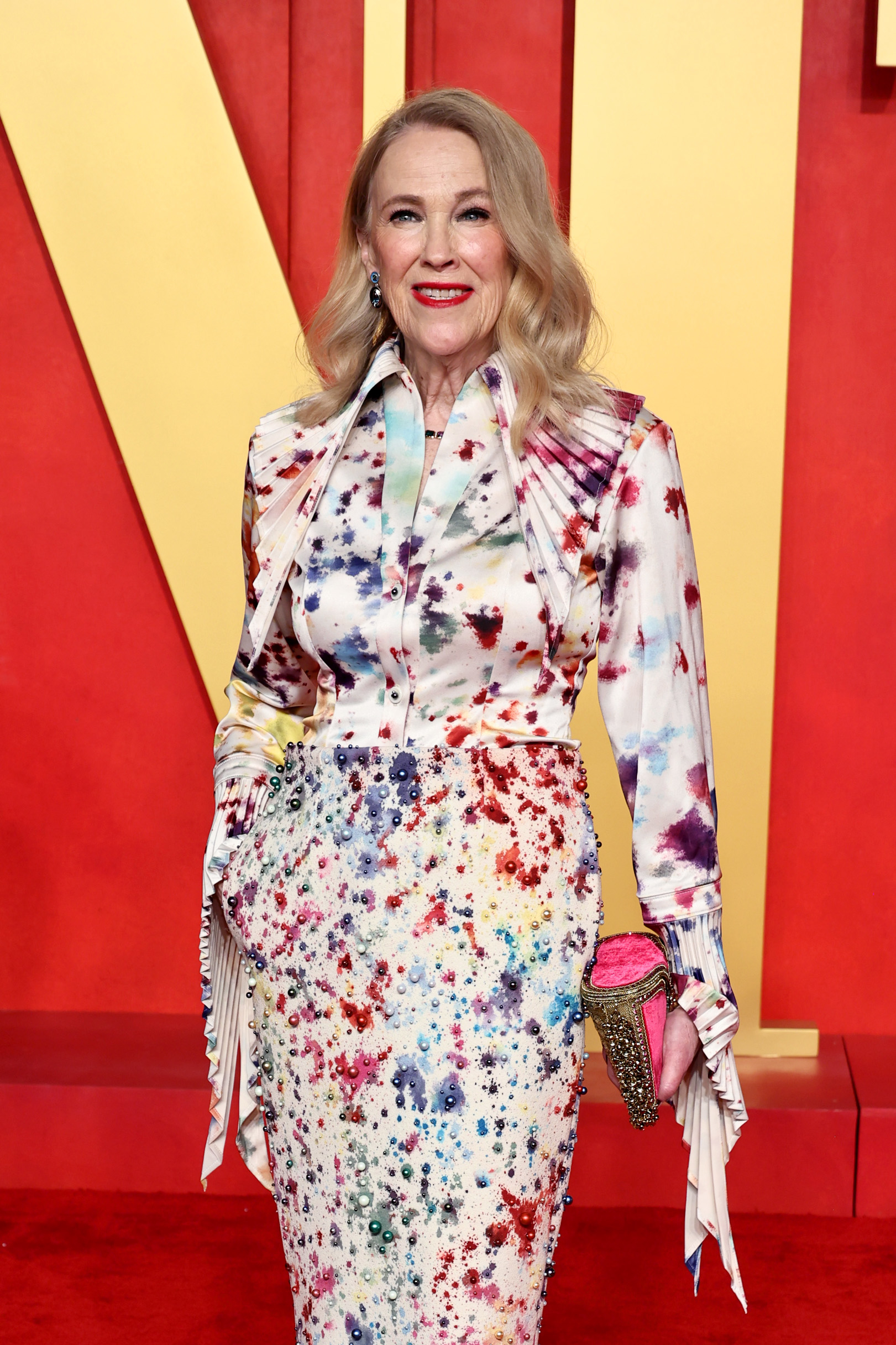 Woman in a painterly splattered suit with a bow tie blouse and embellished clutch posing on red carpet
