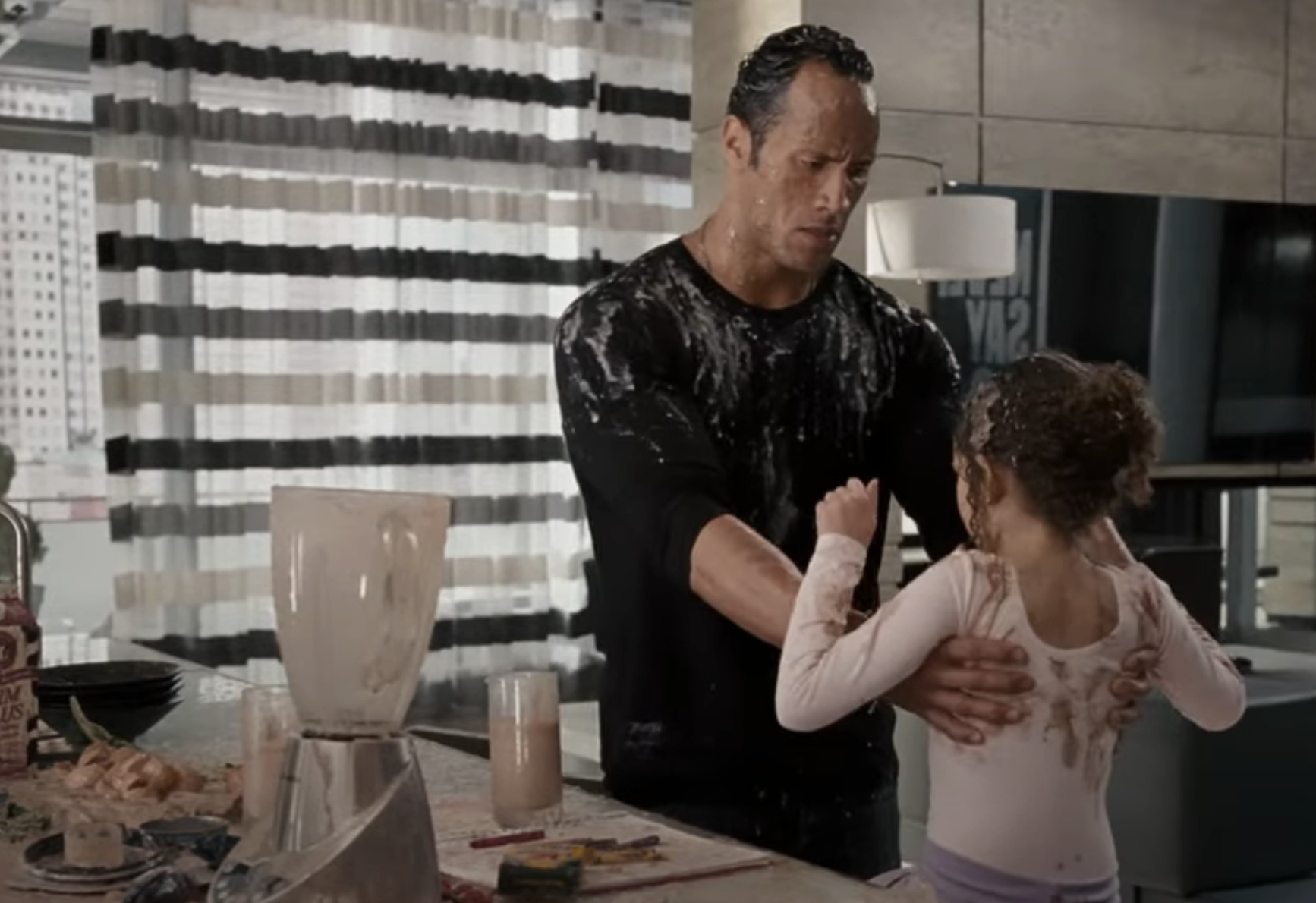 Dwayne Johnson and a young girl in a messy kitchen with splattered food, portraying a playful and chaotic cooking scene